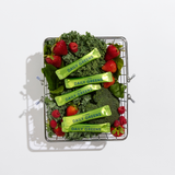 Basket filled with green vegetables and strawberries, with 'Daily Greens' packages on a white background